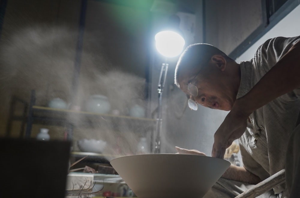 ↑ 在景德鎮(zhèn)，手工匠人吹去坯內(nèi)的泥土（2021年7月14日攝）。