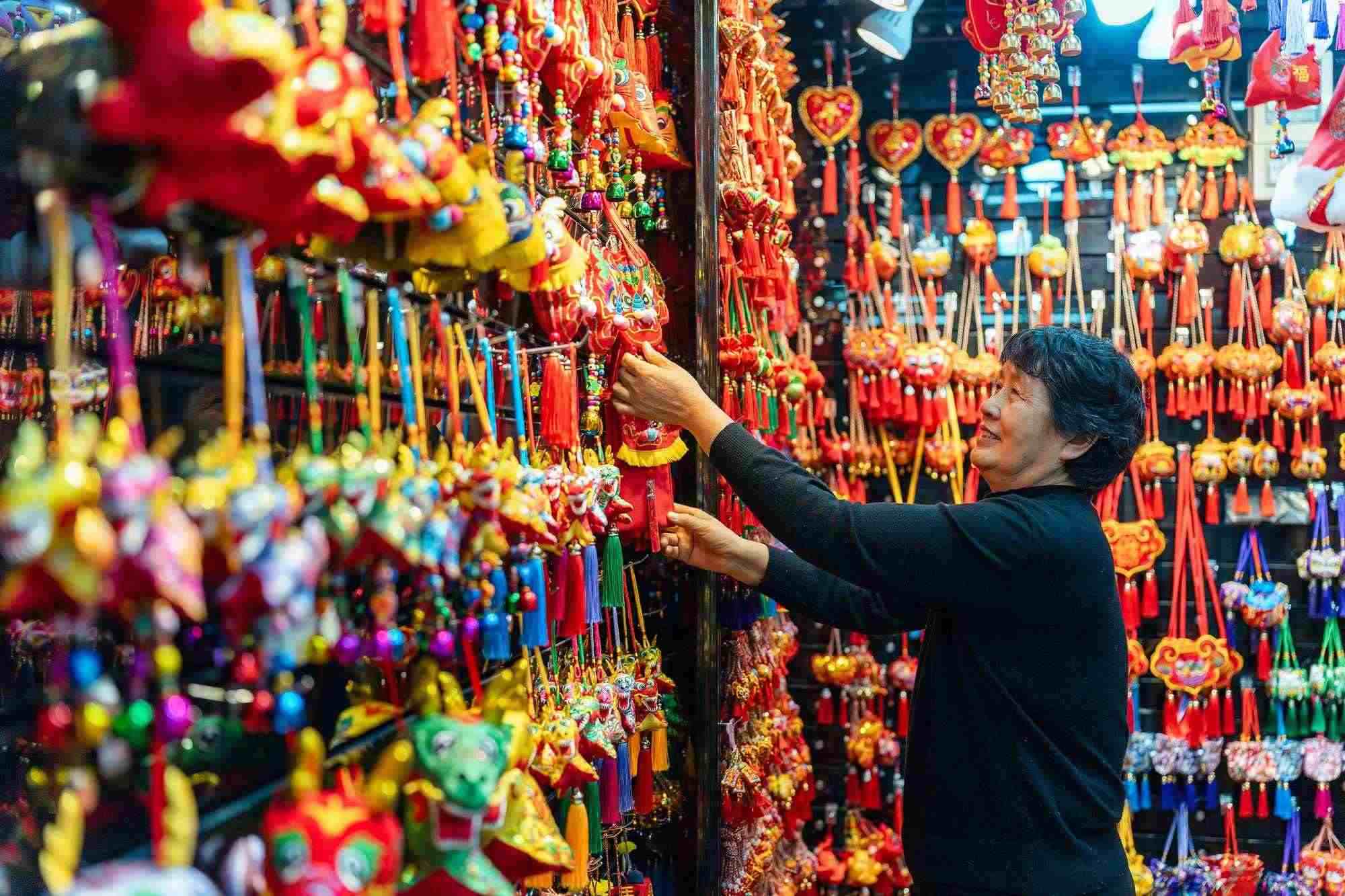 2023年12月11日，金華義烏國(guó)際商貿(mào)城，龍年喜慶用品掛滿攤位，顧客正在挑選中。