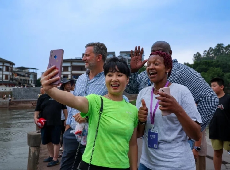 2024“一帶一路”媒體合作論壇聯(lián)合采訪調(diào)研行成員在樂山蘇稽古鎮(zhèn)與游客合影留念。本報(bào)記者 伊霄攝