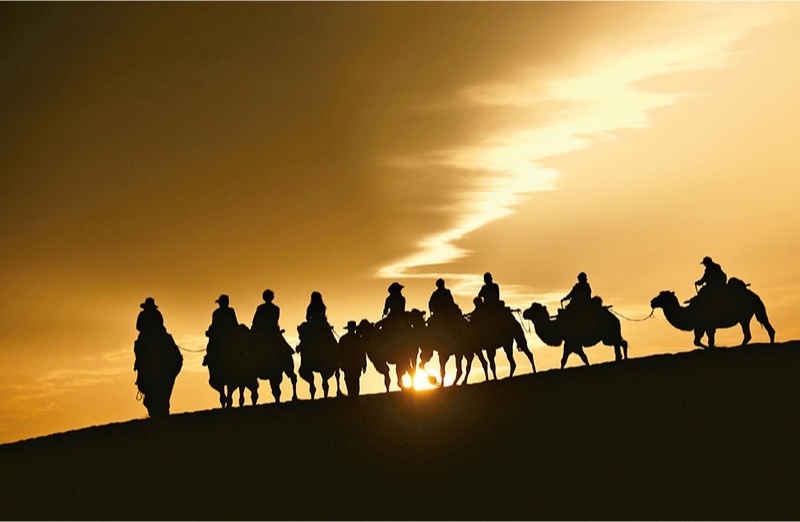 新時(shí)代以來(lái)，文化和旅游深度融合發(fā)展體制機(jī)制不斷健全，成功走出了一條獨(dú)具特色的中國(guó)旅游發(fā)展之路。圖為2024年9月1日清晨，游客在甘肅省敦煌市鳴沙山月牙泉景區(qū)乘騎駱駝，欣賞大漠風(fēng)光，體驗(yàn)絲路風(fēng)情。 新華社發(fā) 張曉亮/攝